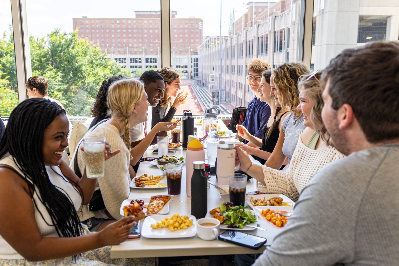 Students laughing together over lunch in a sunlit campus dining hall
